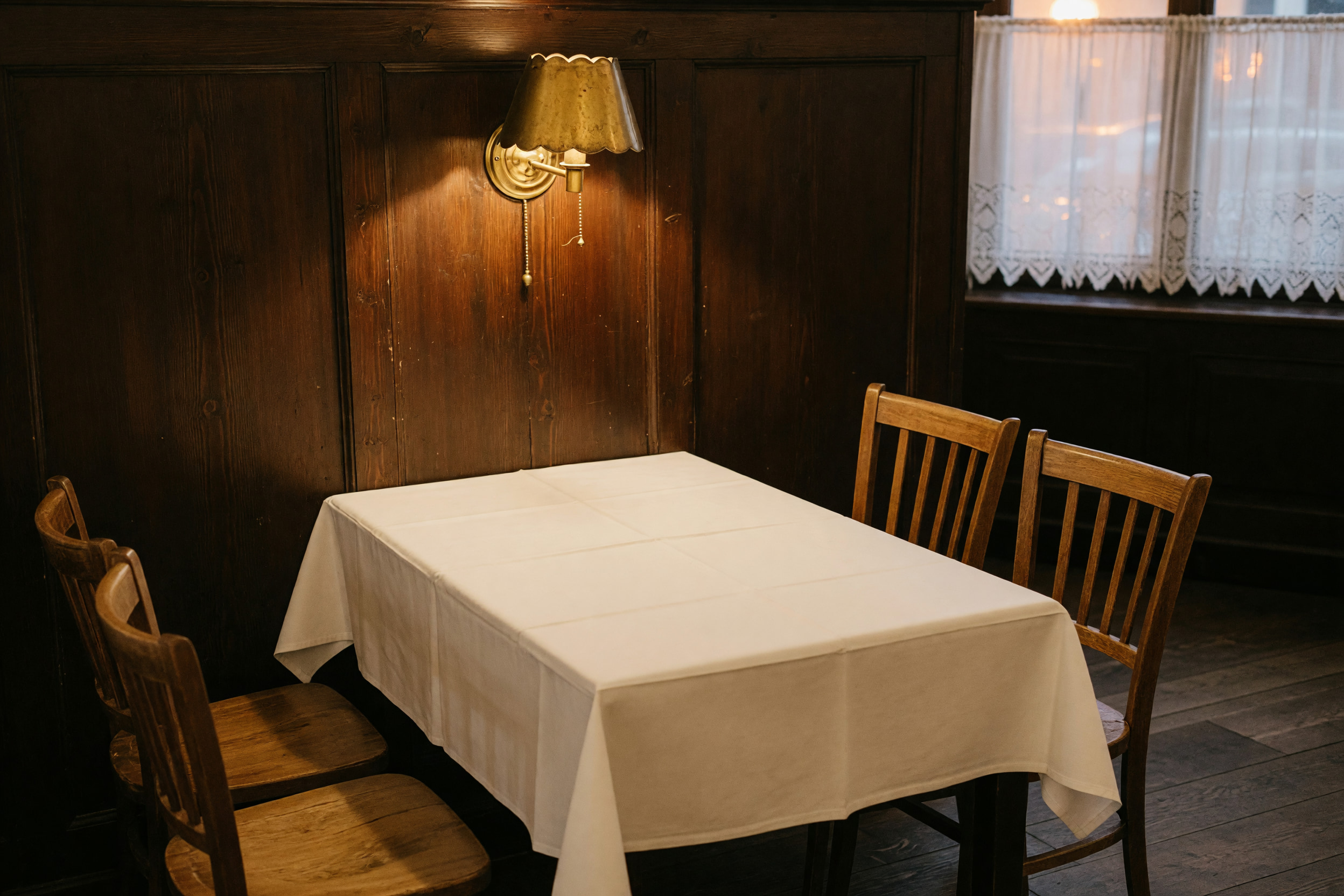 Warm lampenbeleuchteter Schankraum mit dunkler Holzvertäfelung und gedecktem Tisch mit weißem Leinen.